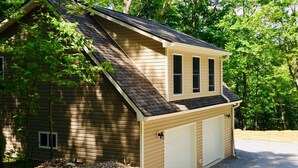 Un bâtiment à deux étages, doté d’un toit à pignon, d’un garage et d’un petit abri attenant.