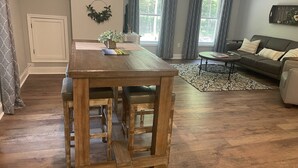 Une table à manger en bois, des tabourets de bar, un canapé et une petite table ronde avec des livres et une lampe.