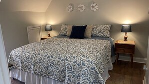 Une chambre à coucher avec un grand lit, deux tables de chevet avec des lampes, une literie à motifs et des œuvres d’art décoratives au mur.