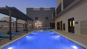 A swimming pool with a blue mosaic floor, surrounded by lounge chairs and a pergola.