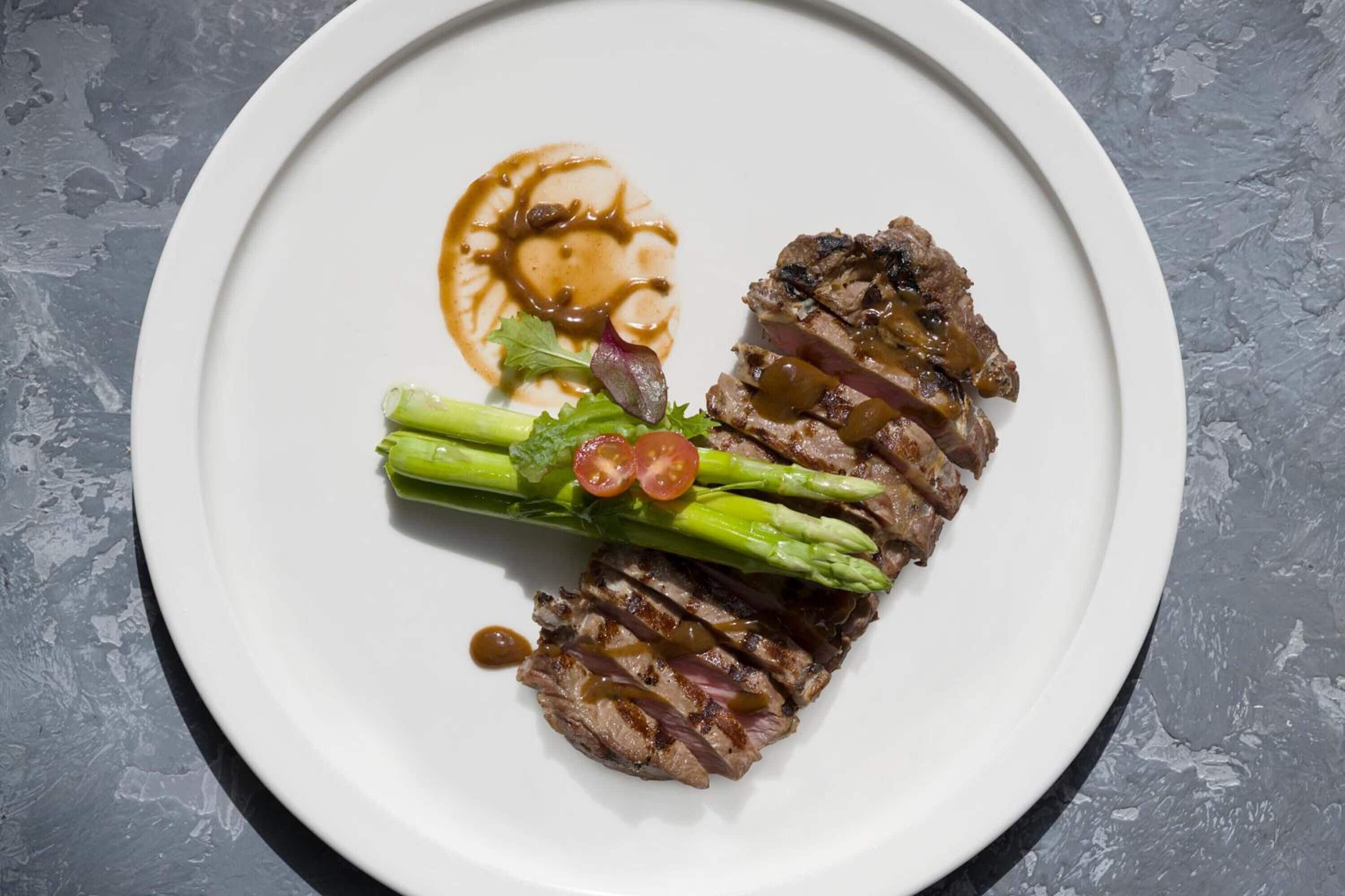 A plate of steak with asparagus and cherry tomatoes, served on a white plate.