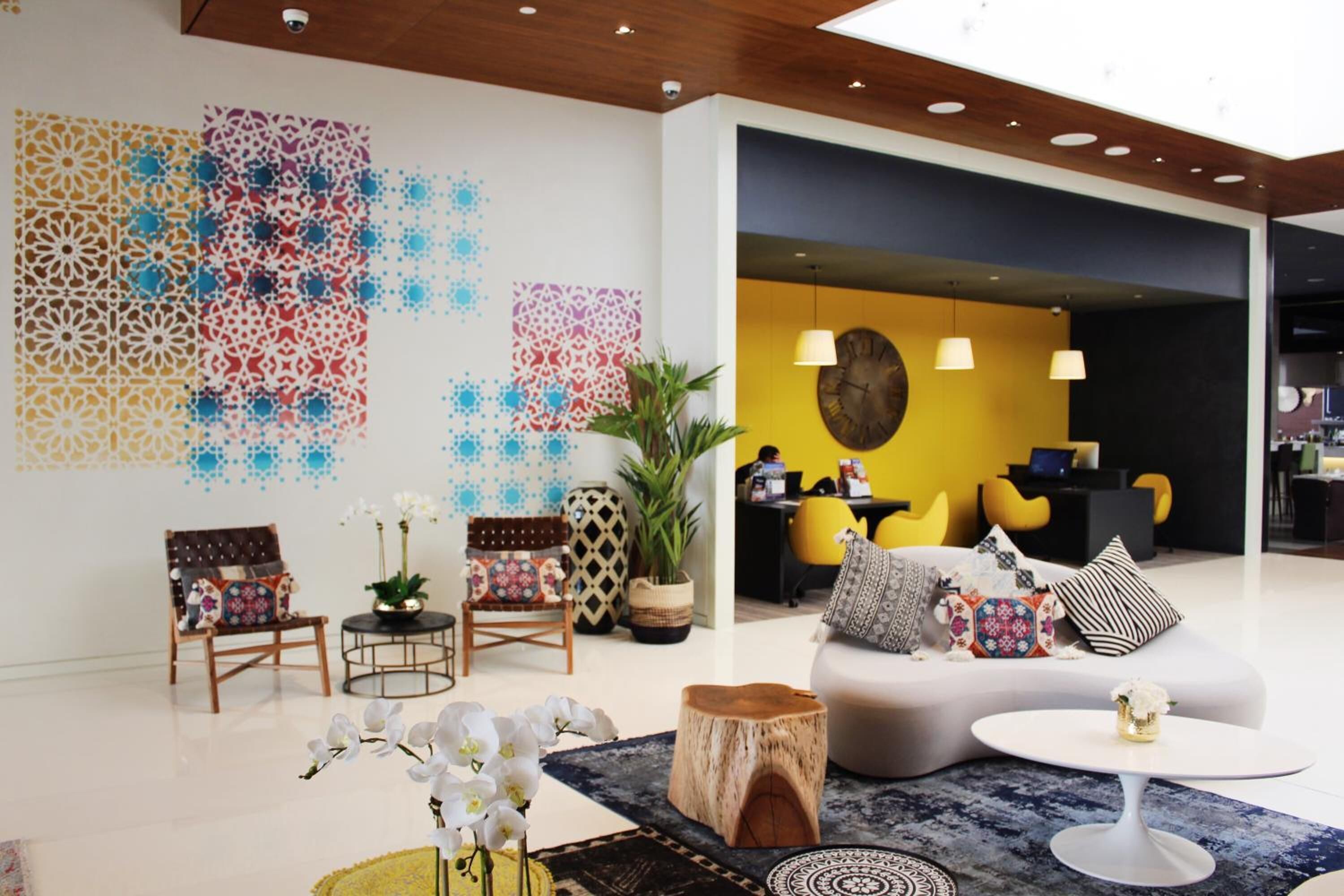 A modern living room with a sofa, chairs, and a coffee table. There is a large wall with decorative patterns and a clock.