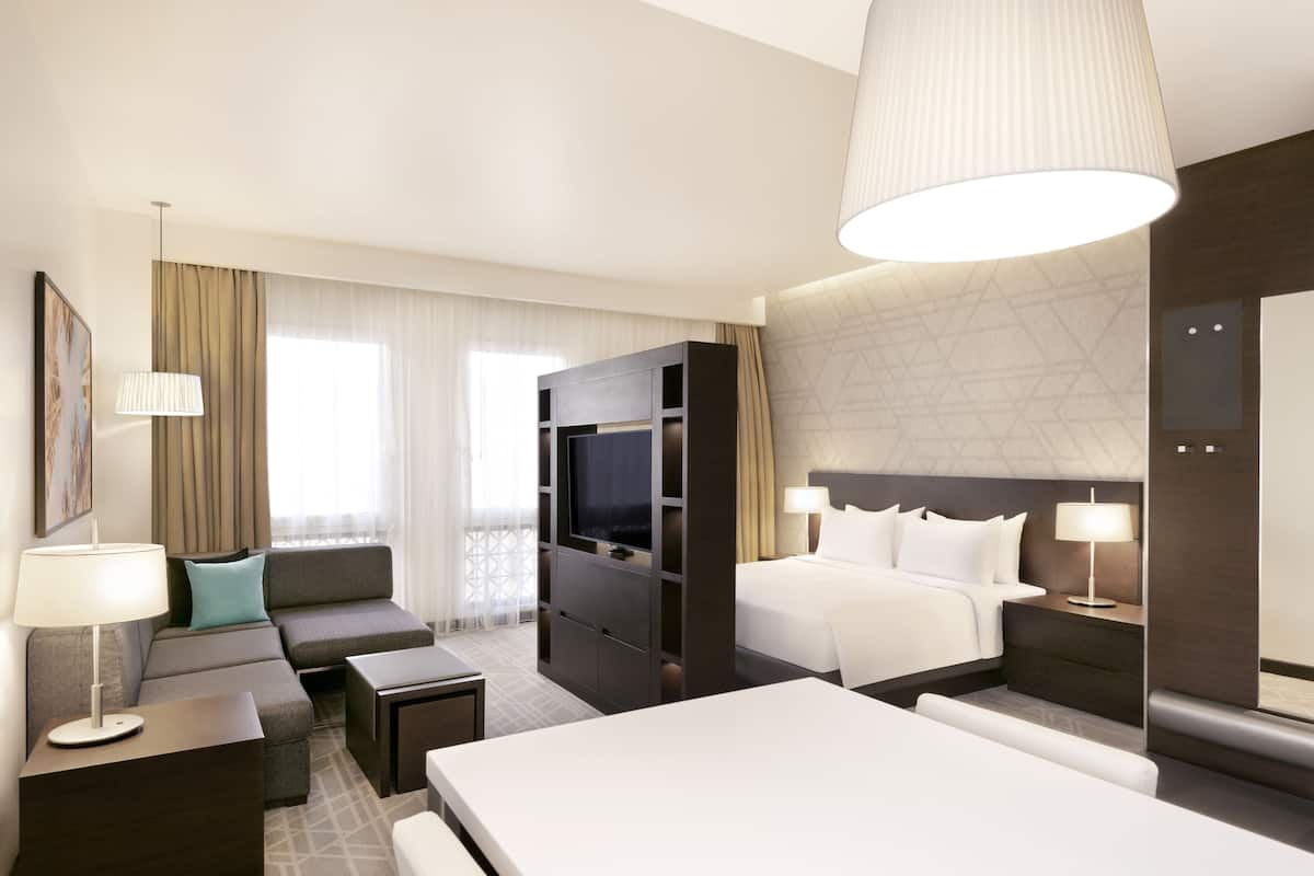 A modern hotel room with a large bed, a sofa, a TV, and a desk.
