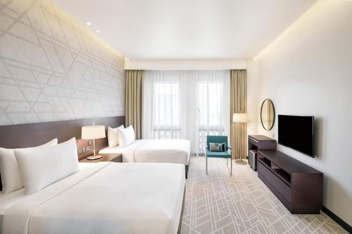 A hotel room with two beds, a TV, a desk, and a balcony.