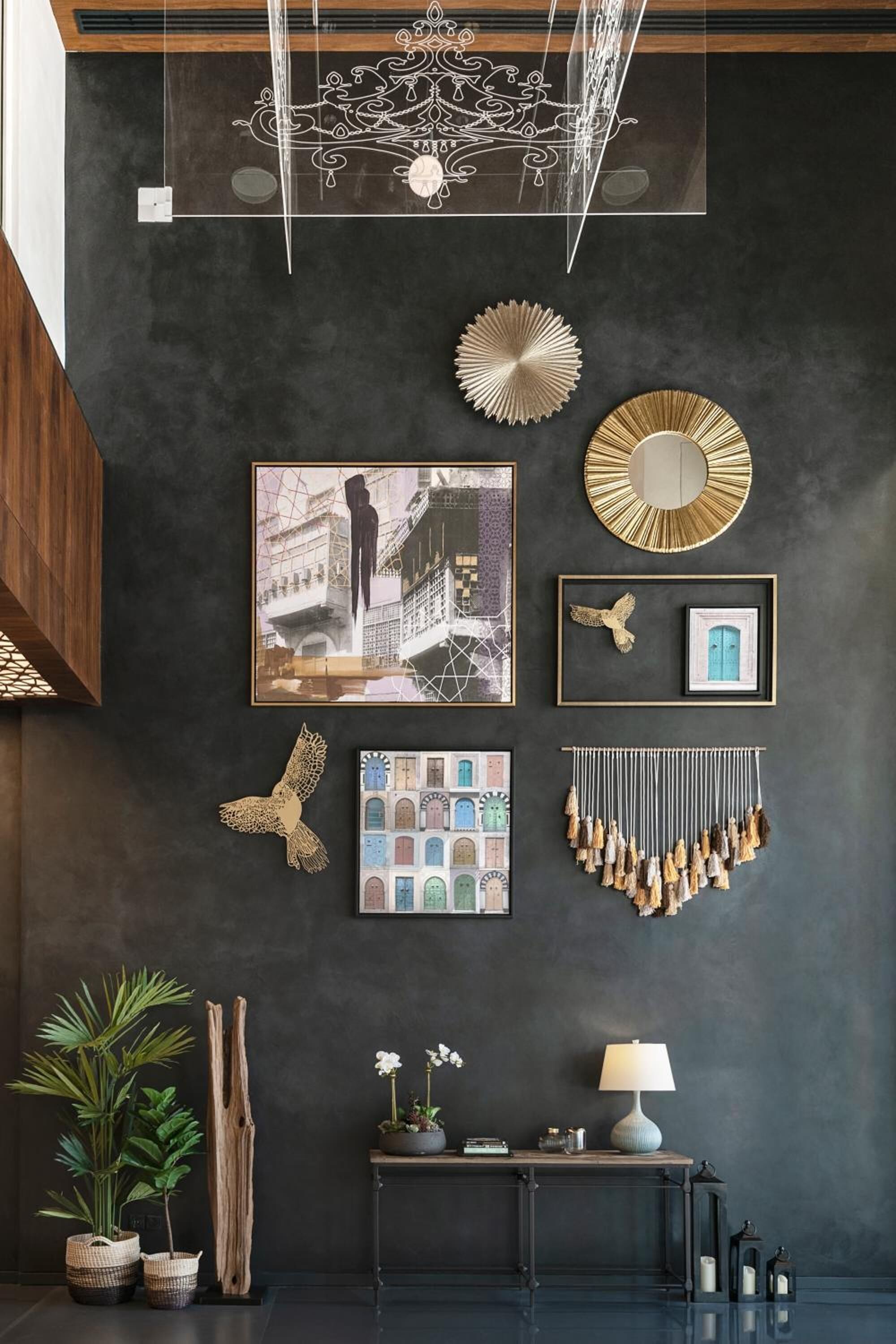 A modern interior with a dark wall, decorative wall art, a hanging light fixture, and a small table with a lamp and plants.