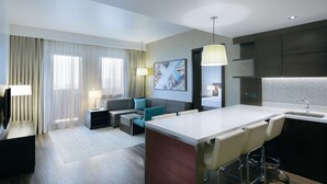 A modern hotel room with a large dining area, a sofa, a TV, and a kitchen with a sink.