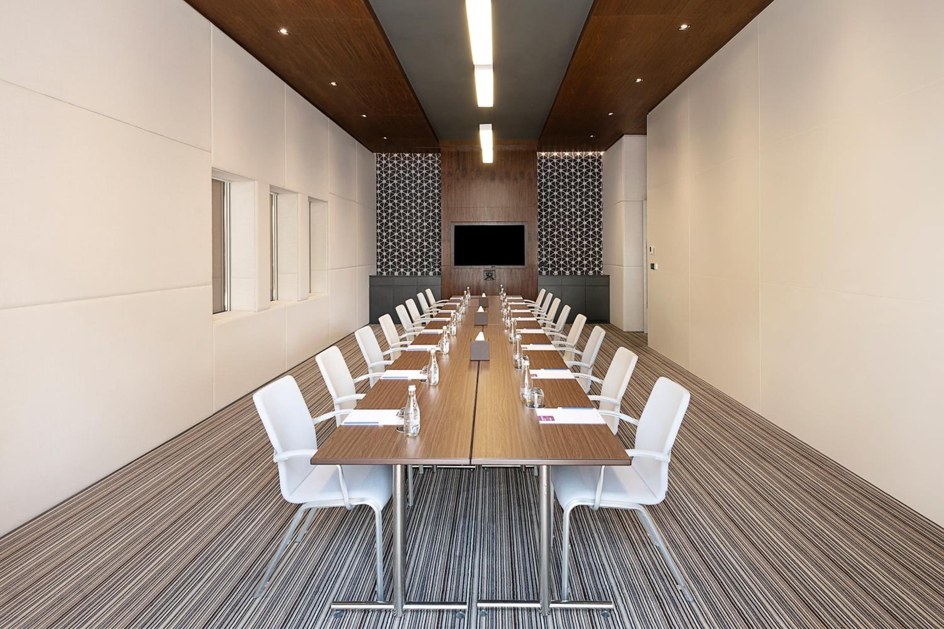 A conference room with a long table, white chairs, and a large screen.