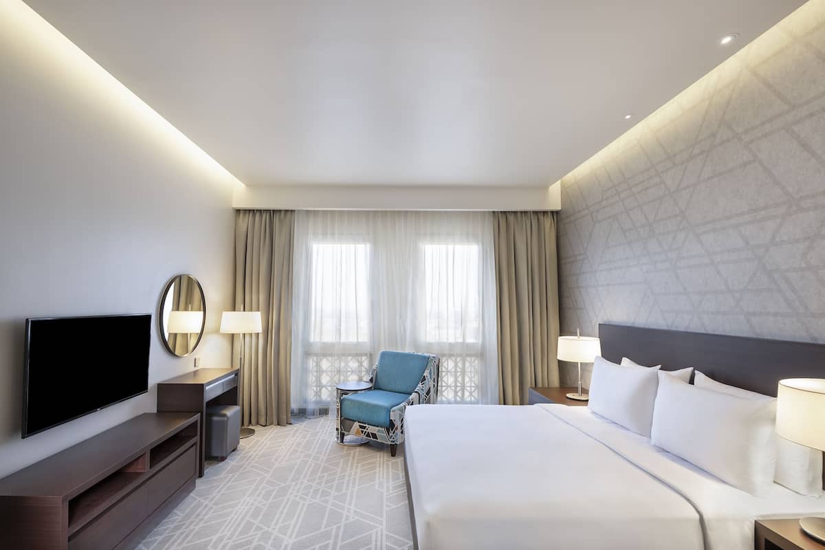 A hotel room with a large bed, a flat-screen TV, a seating area with a chair, and two lamps.