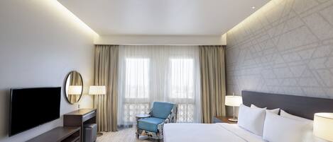 A hotel room with a large bed, a flat-screen TV, a seating area with a chair, and two lamps.