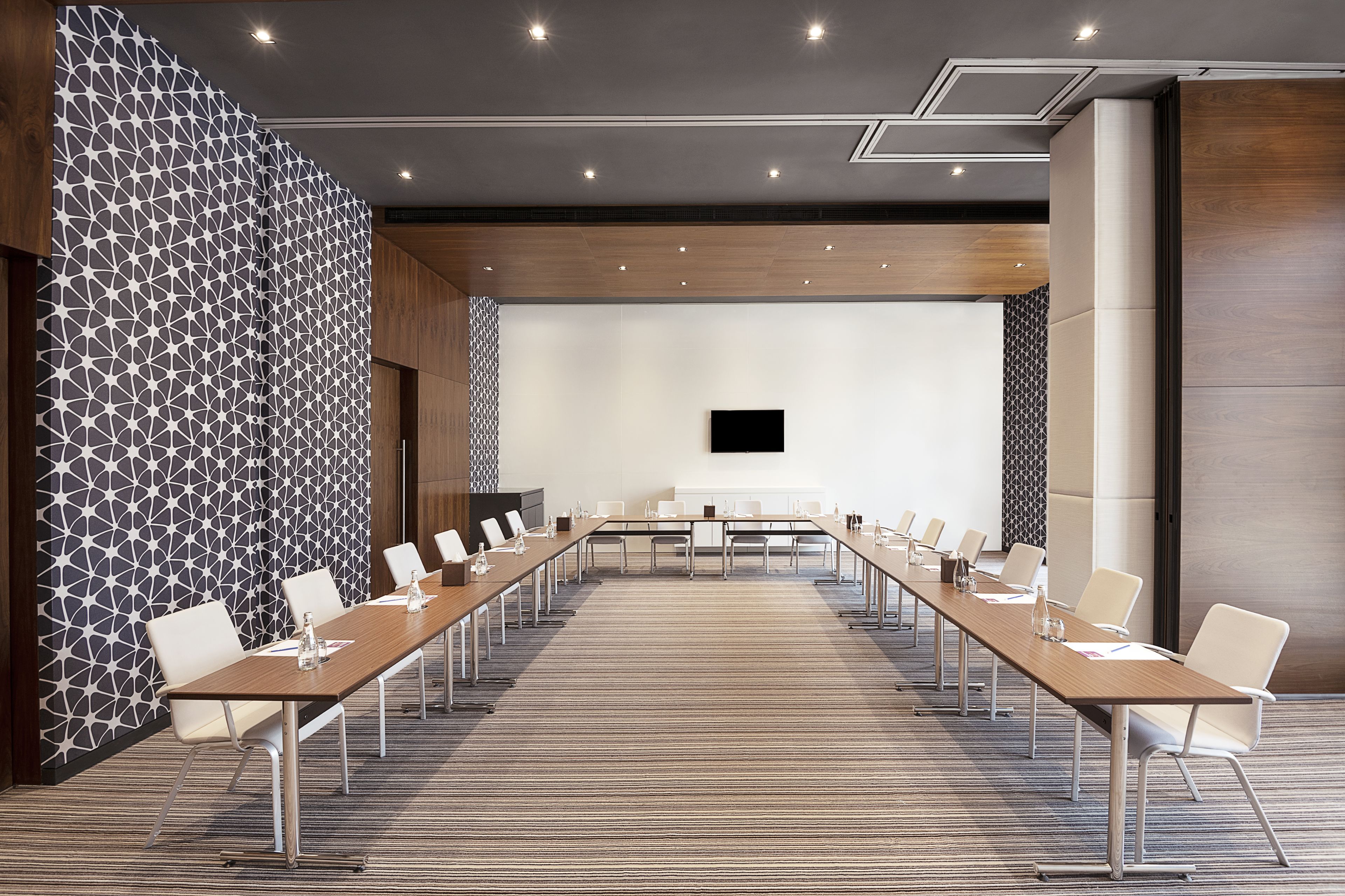 A conference room with a long table, white chairs, and a flat-screen TV.