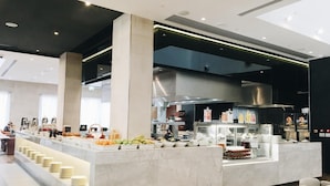 A modern hotel lobby with a central island featuring a buffet, seating area, and a kitchen in the background.