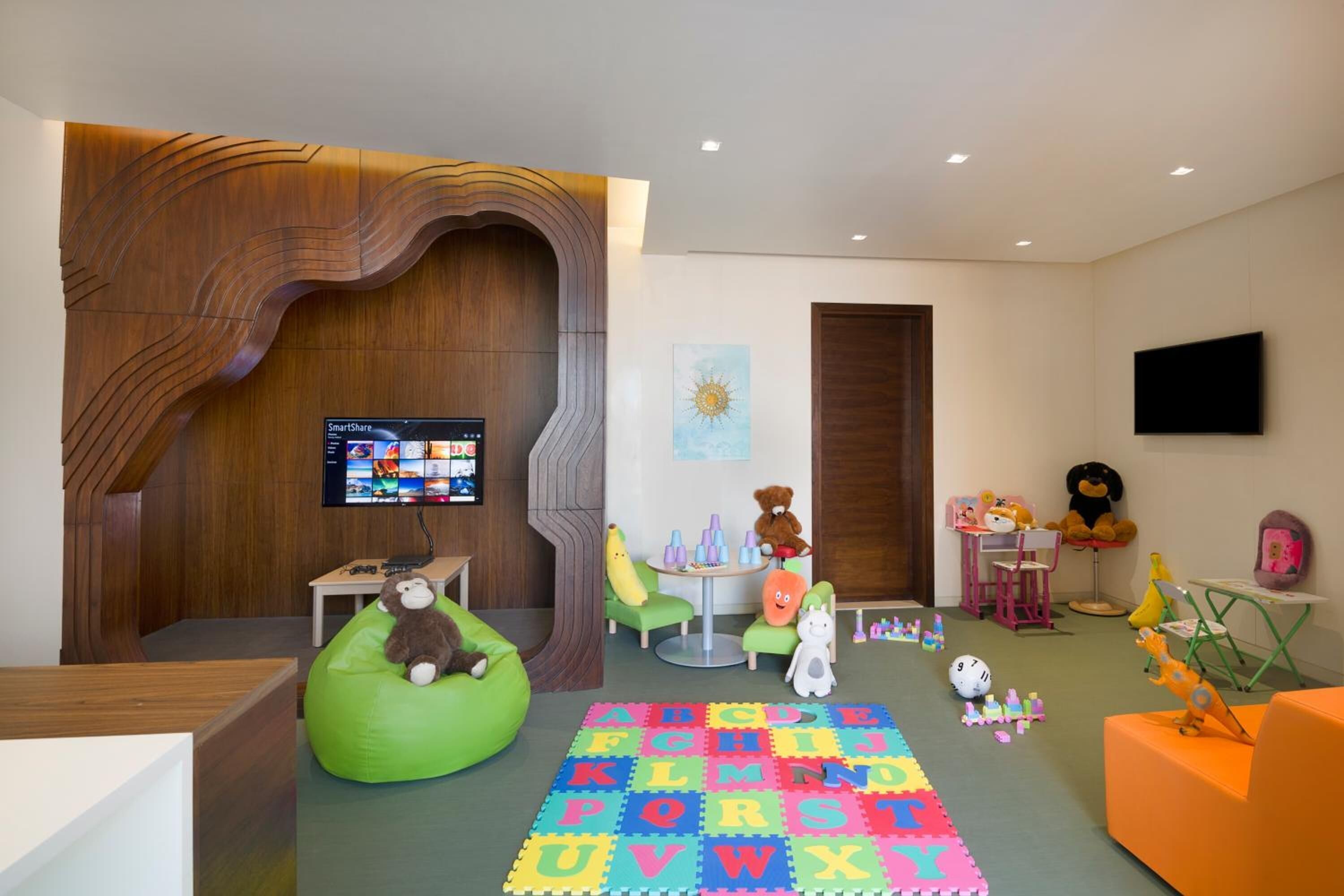 A children's play area with a large alphabet puzzle mat, bean bag chairs, and various toys.