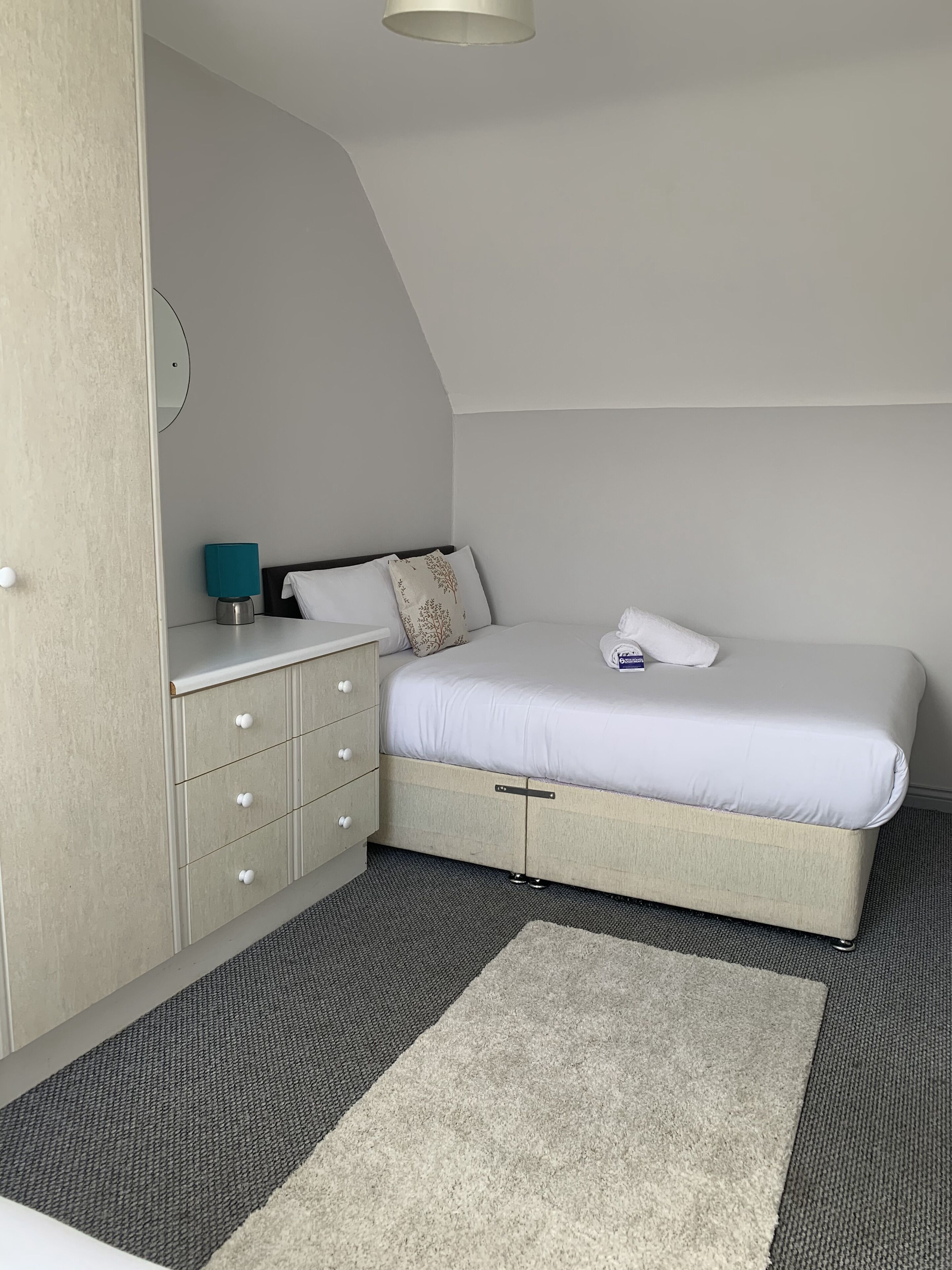 A bedroom with a bed, a dresser, a nightstand, and a small table with a lamp.