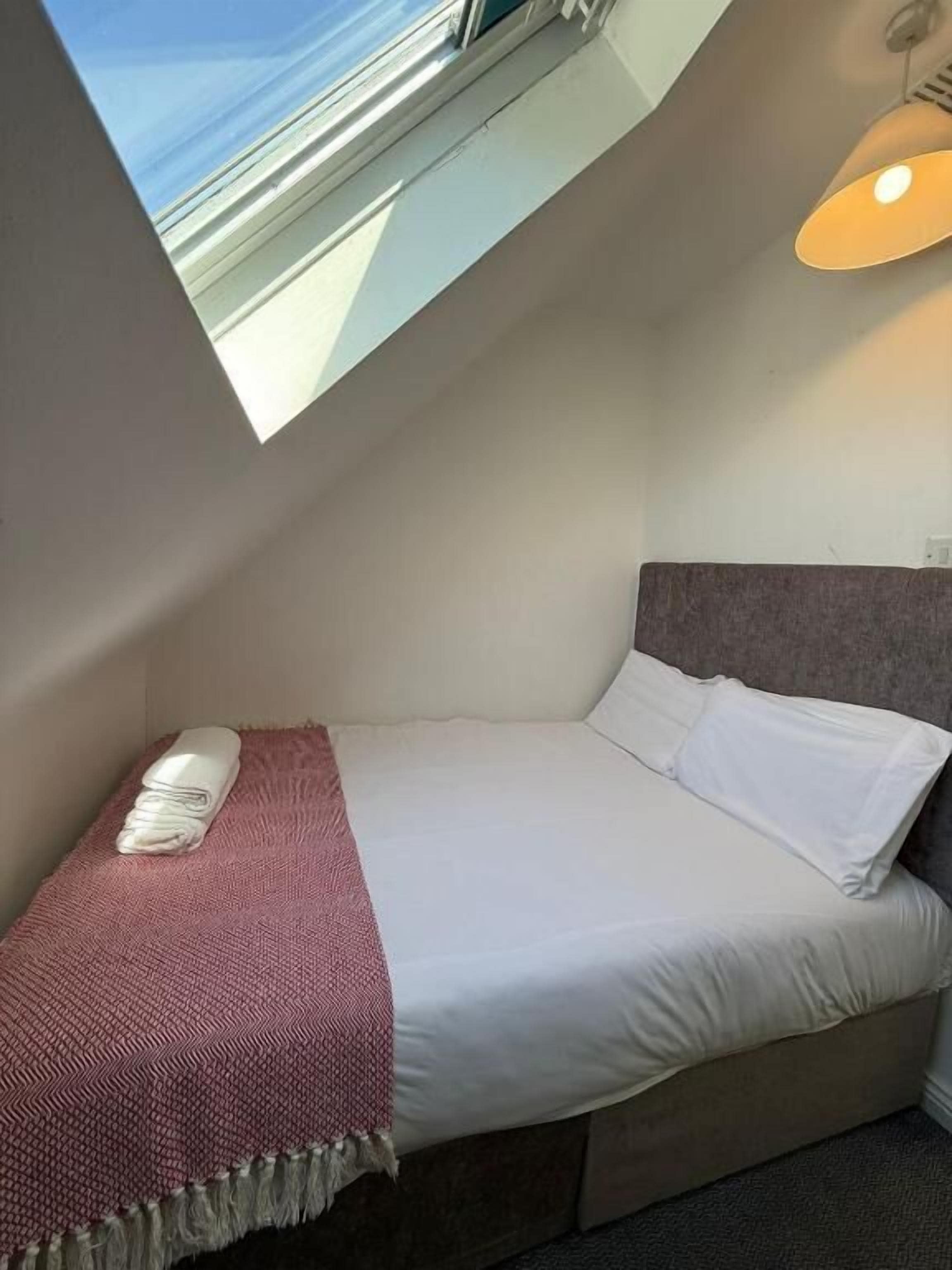 A small, cozy bedroom with a single bed, a red throw blanket, and a view of the sea through a skylight.