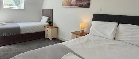 Une chambre d’hôtel avec deux lits, une lucarne, un tableau représentant un paysage urbain et une lampe de chevet.