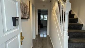 A hallway with a wooden floor, a white door with a brass handle, and a staircase with white balusters.