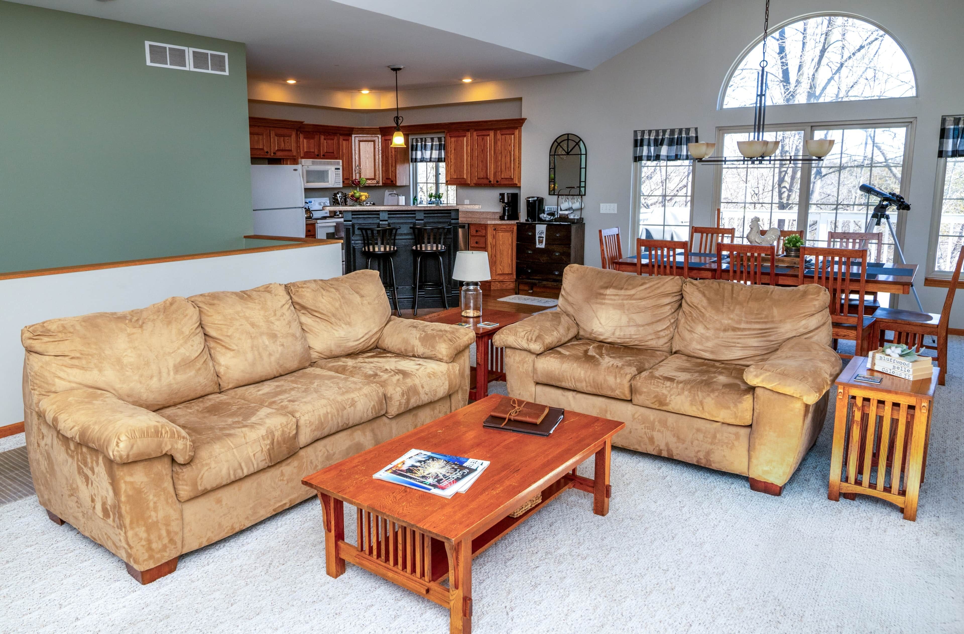A living room with two beige sofas, a wooden coffee table, and a dining area with wooden chairs and a table.