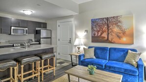 A modern kitchen with stainless steel appliances, a bar area with stools, a blue sofa, and a painting of a sunset.