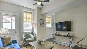 A living room with a ceiling fan, a flat-screen TV, a blue sofa, a light-colored armchair, a coffee table, and a patterned rug.
