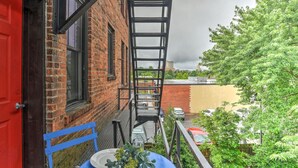 A red door, a brick building, a metal fire escape, and a tree with green leaves.