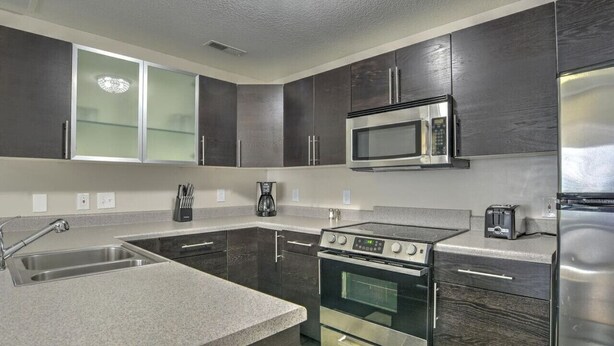 A modern kitchen with dark cabinetry, a stainless steel refrigerator, a microwave, a stove, and a sink.
