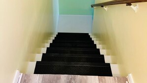 Un escalier avec des marches noires et des contremarches blanches, menant à un palier doté d’un plafond blanc.