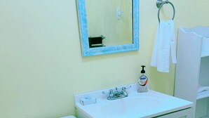 Une salle de bain avec des toilettes blanches, un lavabo doté d’un distributeur de savon et un miroir.