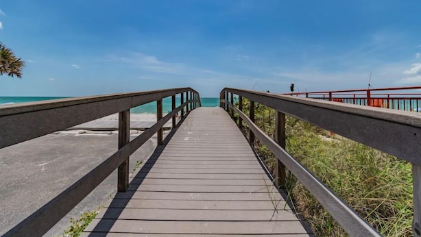 Une promenade en bois qui mène à une plage, avec un ciel bleu dégagé.