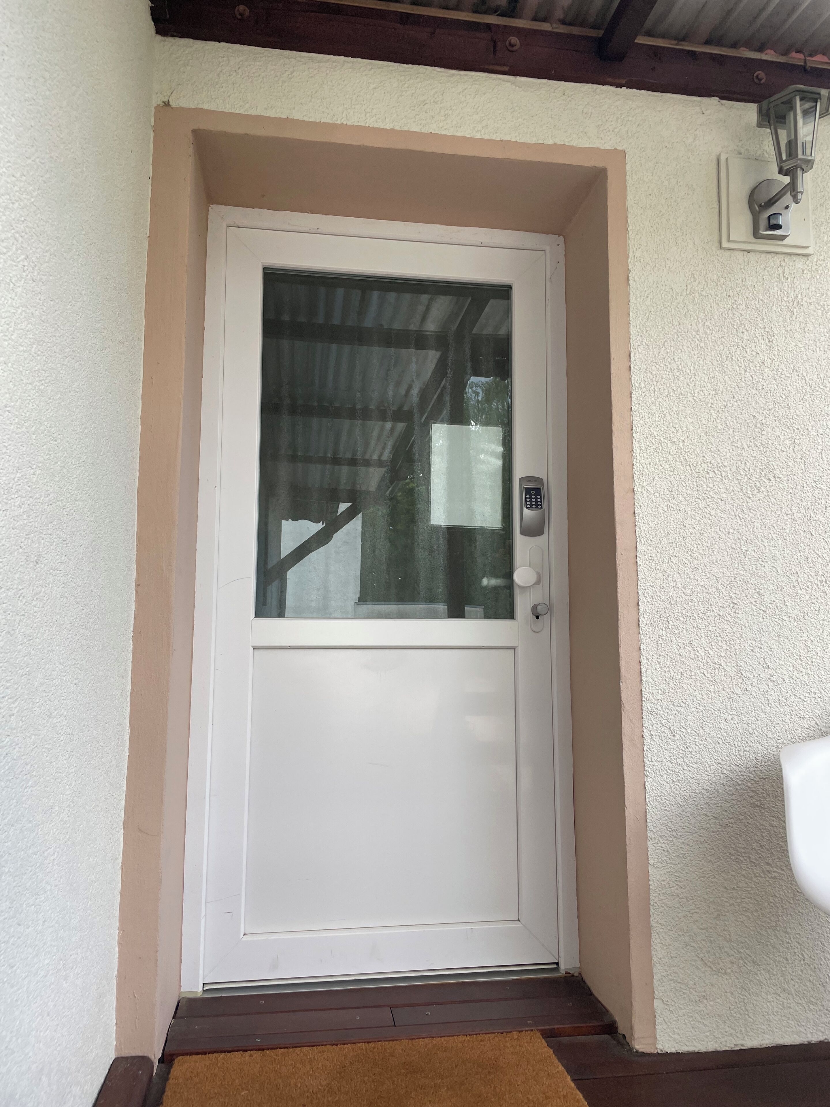Eine weiße Tür mit Fensterteil, einem Zahlenschloss und einer kleinen Stufe.