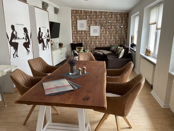 A modern dining area with a wooden table and brown upholstered chairs, a patterned wallpaper, and a cozy seating area with a sofa and cushions.