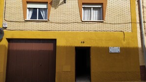 A yellow building with a large garage door, two windows with curtains, and a sign indicating the address.