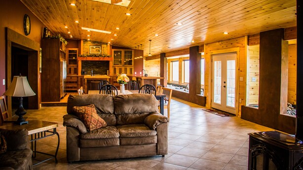 Interior acogedor de una cabaña con techo de madera, chimenea, comedor y sala de estar con sofá.