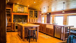 Una cocina con armarios de madera, una isla central con taburetes, horno empotrado e iluminación colgante.