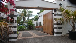 Une entrée fermée par un portail, avec un chemin pavé menant à un bâtiment dont la façade est décorée de rayures noires et blanches.