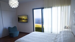 Une chambre à coucher avec un lit, une chaise, un tableau et une vue sur la mer, visible à travers une grande fenêtre.