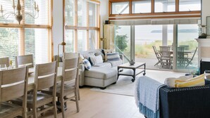 A spacious living area with a sofa, chairs, and a dining table. Large windows offer a view of the outdoors. - Beachfront Getaway in Semiahmoo (Blaine)