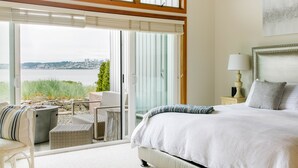 A bedroom with a large bed, a nightstand, a lamp, and a view of a body of water through a sliding glass door. - Beachfront Getaway in Semiahmoo (Blaine)
