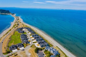 Vista aérea de una zona residencial costera con casas a lo largo de la playa, aguas azules cristalinas y una carretera serpenteando por la propiedad.