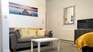 A modern living room with a grey sofa, a white coffee table, a black TV stand, and a yellow throw blanket. - Toothbrush Apartments - Central Ipswich East - Rope Walk (Ipswich)