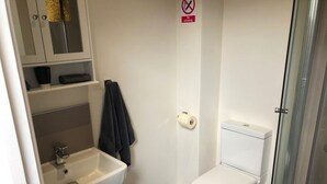 A small, clean bathroom with a white sink, toilet, and shower. There is a towel hanging on the wall and a 'No Smoking' sign above the toilet. - Toothbrush Apartments - Central Ipswich East - Rope Walk (Ipswich)