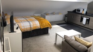 A modern bedroom with a bed, a TV, a desk, a sofa, and a kitchenette. - Toothbrush Apartments - Central Ipswich East - Rope Walk (Ipswich)