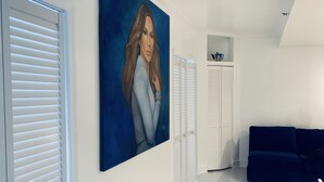 Ein modernes Wohnzimmer mit einem großen Gemälde, weißen Lamellenläden und einem dunkelblauen Sofa.