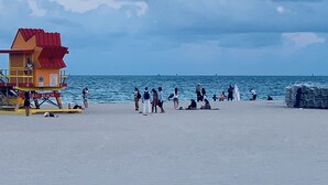 Ein Rettungsschwimmturm und Strandbesucher an einem sandigen Strand mit dem Meer im Hintergrund.