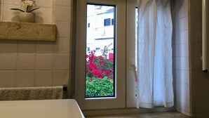Un bagno con una finestra, un porta asciugamani e un piccolo ripiano con fiori.