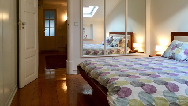 Una camera da letto con un letto, uno specchio grande, un comodino e una porta che dà su un'altra stanza.