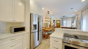 Una cocina moderna con armarios blancos, electrodomésticos de acero inoxidable y una zona de comedor con mobiliario de madera.