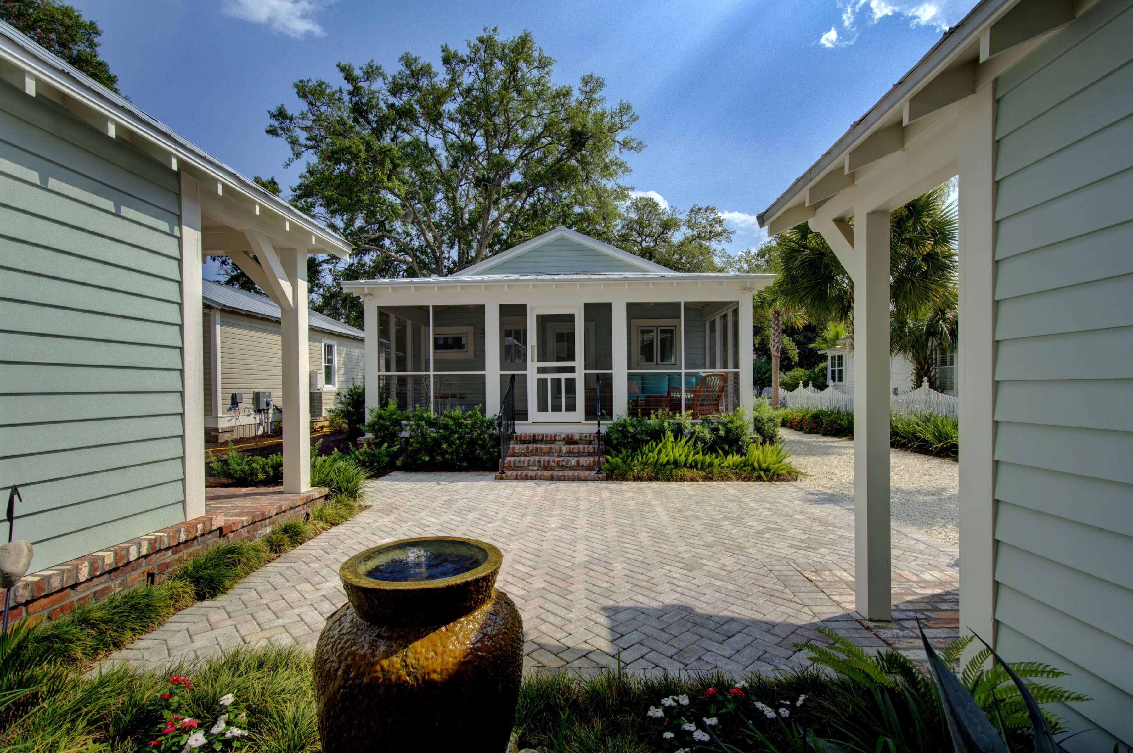 A covered porch with a brick pathway leading to a house with a green roof.