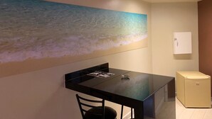 Ein kleines Zimmer mit Esstisch, Stuhl, Klimaanlage, Kühlschrank und einem Wandbild.