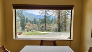 A room with a large window overlooking a forested area with mountains in the background.