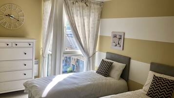 A bedroom with a bed, a dresser, a clock, and a window with curtains.